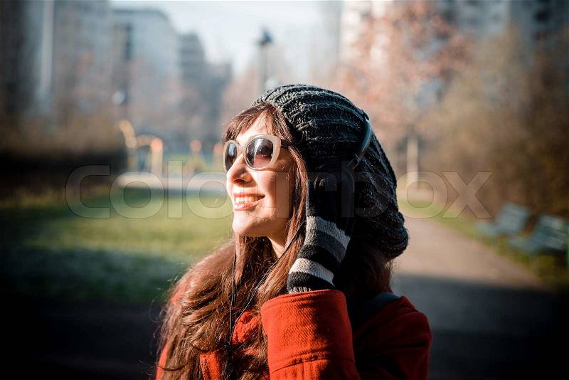 Beautiful woman red coat winter listening music headphones park, stock photo