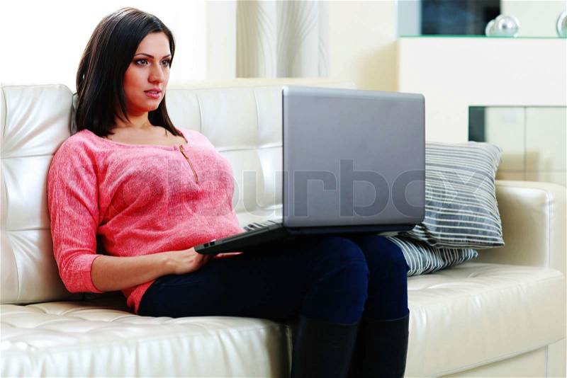 Young beautiful woman sitting on the sofa with laptop at home, stock photo