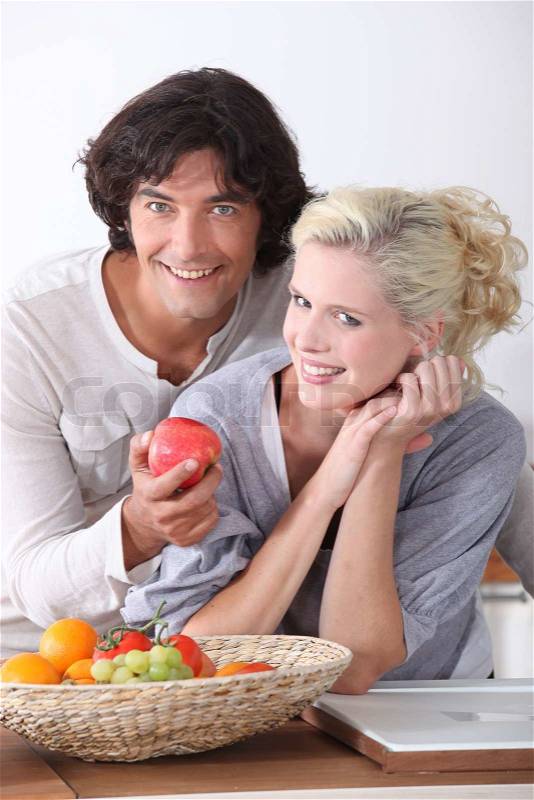 Couple eating fruit from basket in kitchen, stock photo