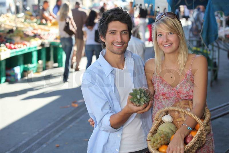 Young couple with a basket of fruit in a busy marketplace, stock photo
