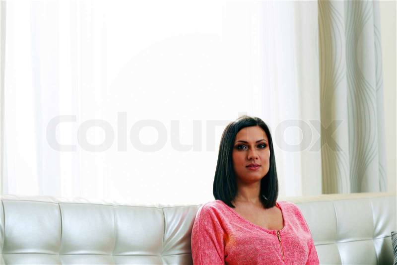 Middle-aged thoughtful woman sitting on the sofa near the big window, stock photo