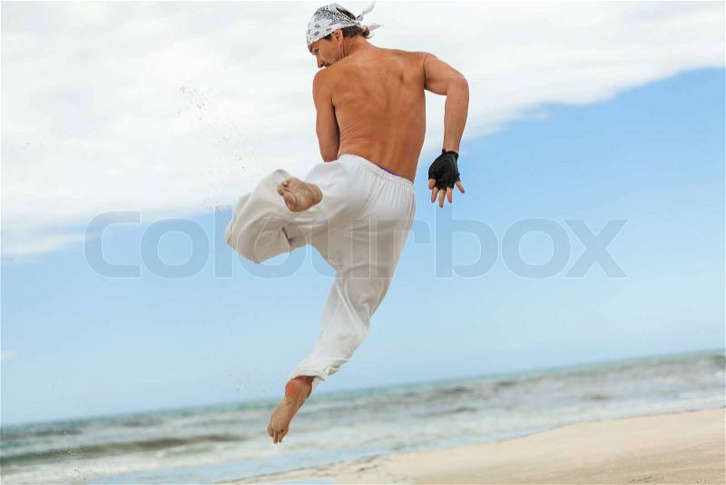 Man is jumping sport karate martial arts fight kick jump beach summertime, stock photo