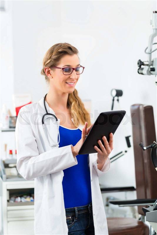 Young female doctor standing in clinic reading a file or dossier on the tablet computer, stock photo