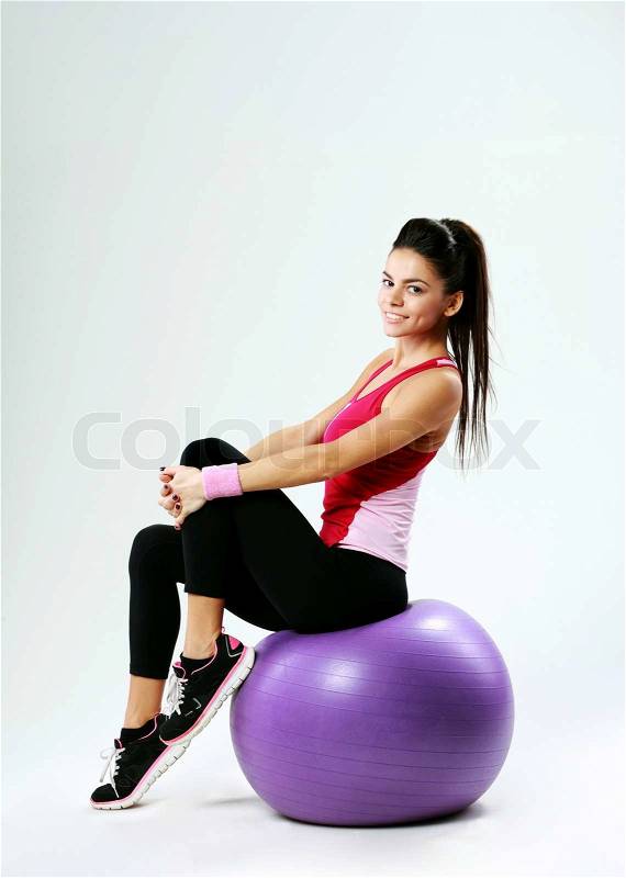 Young happy sport woman sitting on fitball on gray background, stock photo