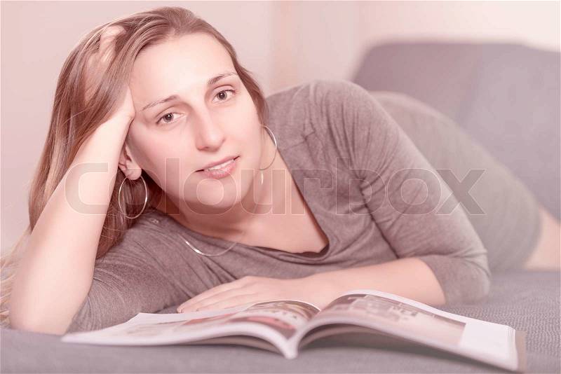 Young woman on the bed reading a magazine, stock photo
