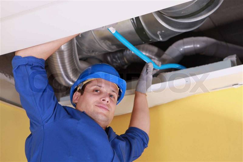 Plumber holding a blue pipe above a ceiling, stock photo