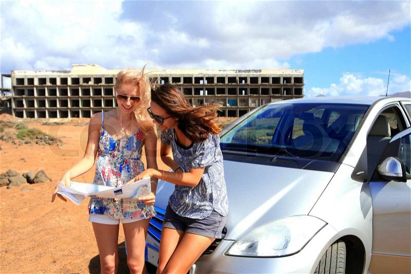 Two young women with car look at road map with old building in background, stock photo