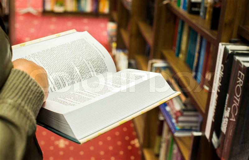 Hand holding open book in a bookstore. Many books on the background, stock photo
