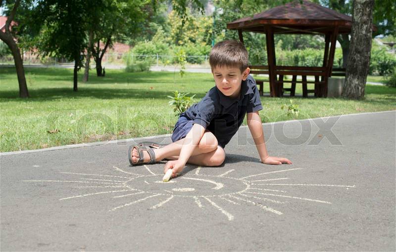 Child drawing sun on asphalt in a park, stock photo
