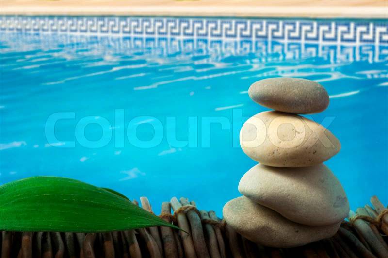 Stacked stones on wooden base for spa and green leaf. Swimming Pool on the background, stock photo