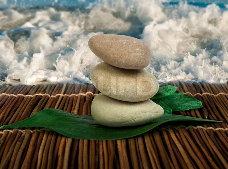 Stacked stones on wooden base for spa and green leafs. Waves on the background, stock photo