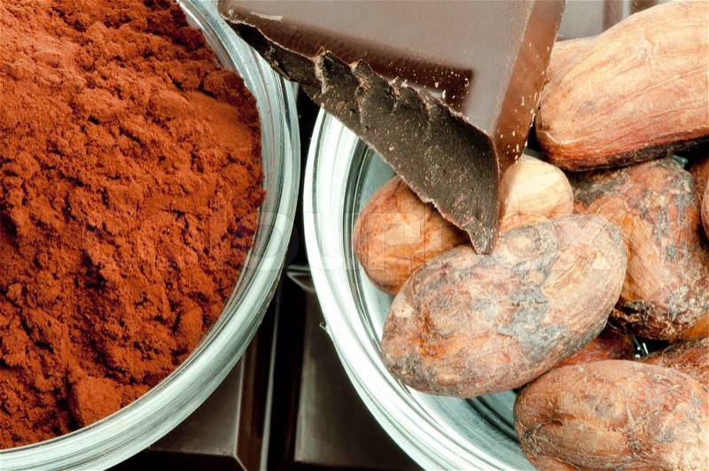 Cocoa beans, cocoa powder in bowls and chocolate bar close up, stock photo