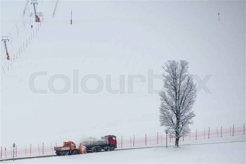 Municipal snow removal crew at work; snow thrower and dump truck on street with skiing slope in the background, stock photo