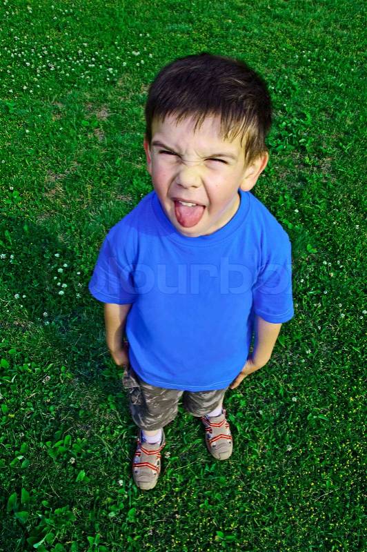 Young boy tongue sticking on green meadow, stock photo