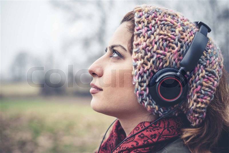 Beautiful brunette woman listening to music with headphones at the park outdoor in winter, stock photo