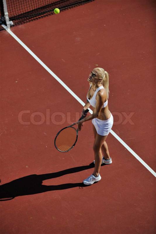 Young fit woman play tennis outdoor on orange tennis field at early morning, stock photo