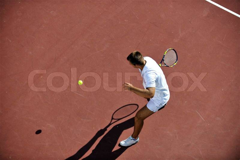 Young man play tennis outdoor on orange tennis field at early morning, stock photo