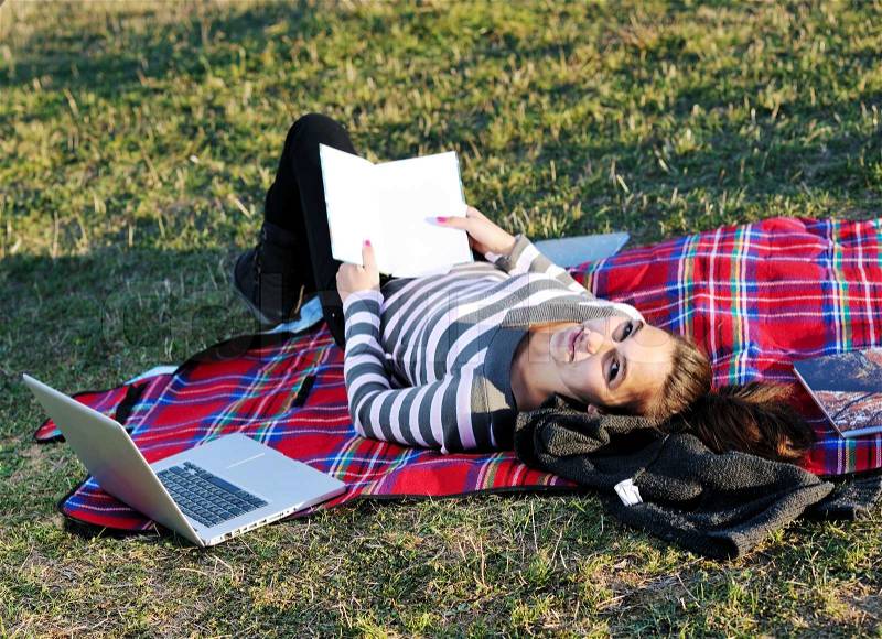 Young teen girl read book and study homework outdoor in nature with blue sky in background, stock photo