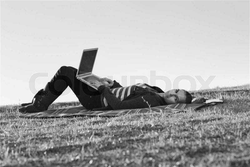 Young teen woman work on laptop computer outdoor in nature with blue sky and green grass in background, stock photo