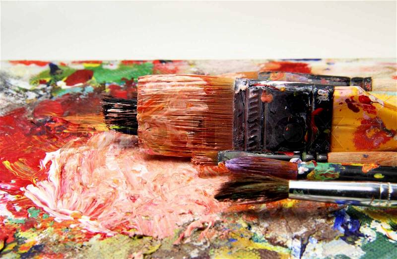Beautiful vivid art palette and mix of paintbrushes in fresh paint, stock photo