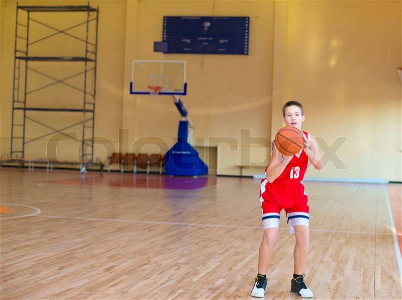 Basketball player with a ball in his hands and a red uniform. Basketball player practicing in the gym, stock photo