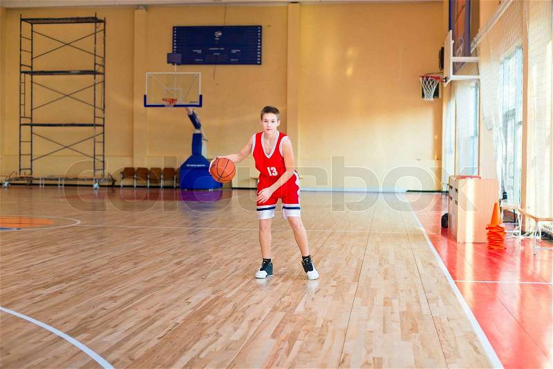 Basketball player with a ball in his hands and a red uniform. Basketball player practicing in the gym, stock photo