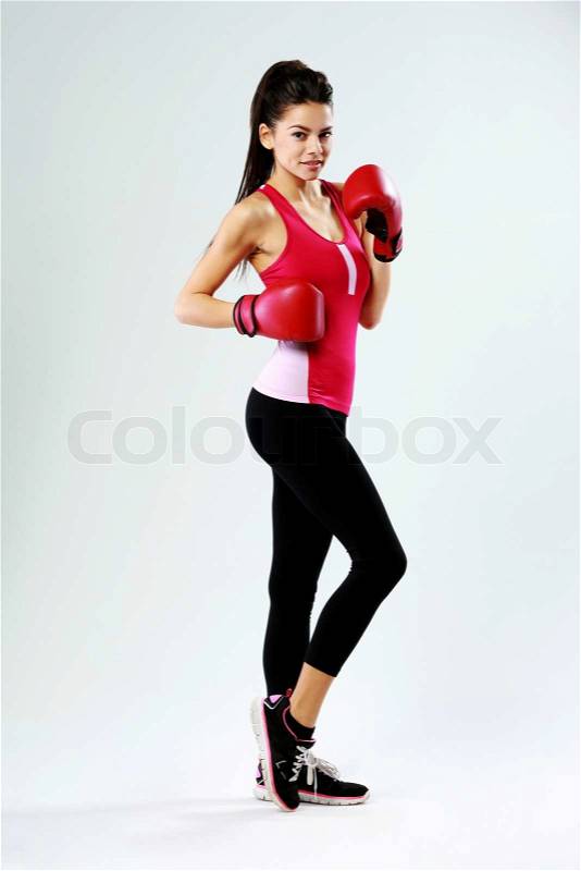 Young happy sports woman standing with boxing gloves on gray background, stock photo