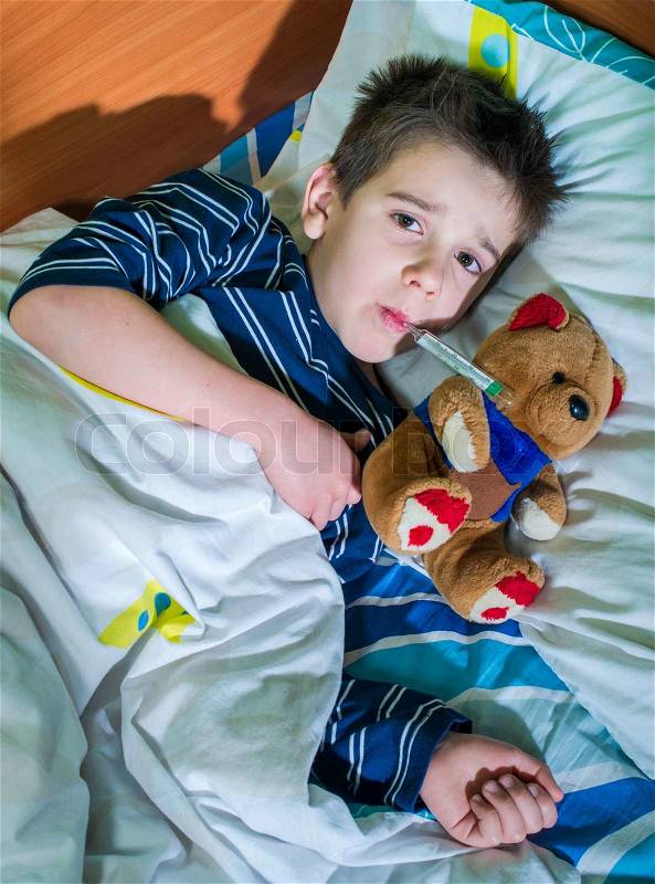 Sick child in bed with teddy bear. Measuring the temperature with a thermometer, stock photo