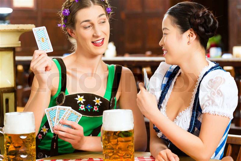 In Pub - friends in Tracht, Dirndl and Lederhosen drinking a fresh beer in Bavaria, Germany playing cards, stock photo