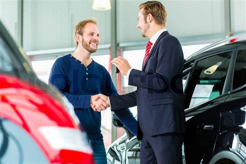 Seller or car salesman and customer in auto dealership, they shaking hands, hands over the car keys and seal the purchase of the auto or new car, stock photo