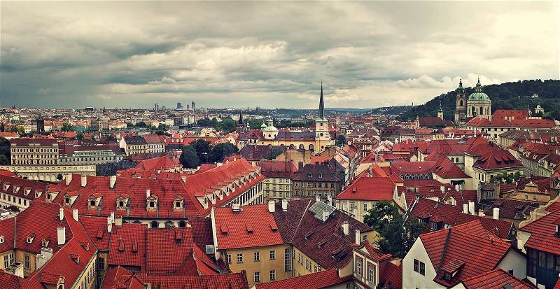 Panoramic view of typical buildings with red roofs in old city under cloudy sky in Prague, Czech Republic (toned), stock photo