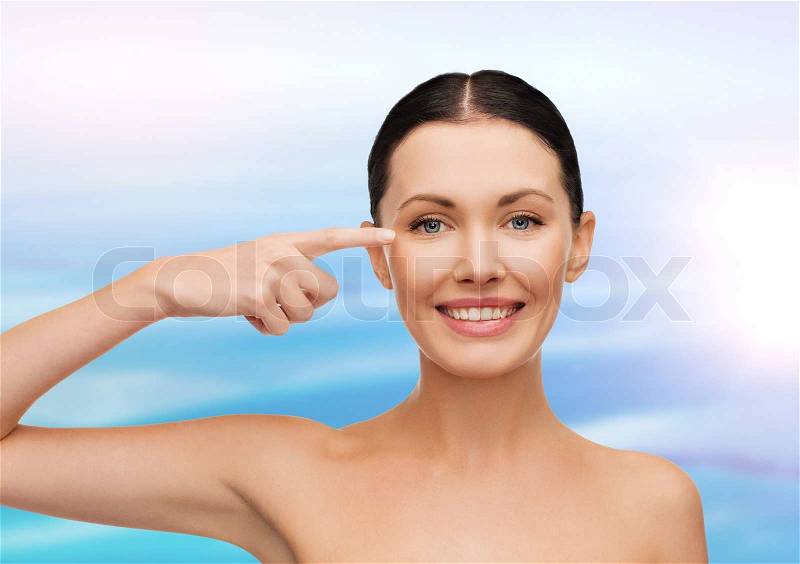 Health, spa and beauty concept - clean face of beautiful young woman pointing to her eye, stock photo