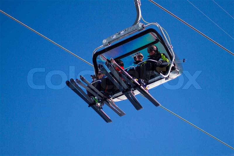 Four skiers sitting in ski lift. Trademarks have been removed, stock photo