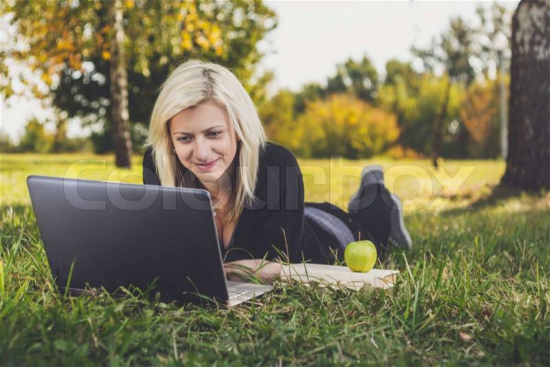 Student girl with laptop studying in the park, stock photo