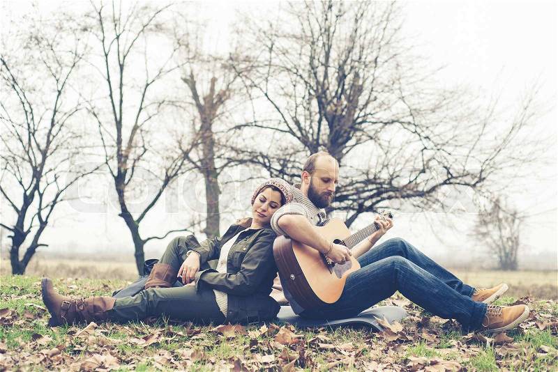 Couple in love playing serenade with guitar at the park winter, stock photo
