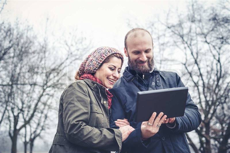 Couple in love using tablet connecting web wireless wifi at the park winter, stock photo