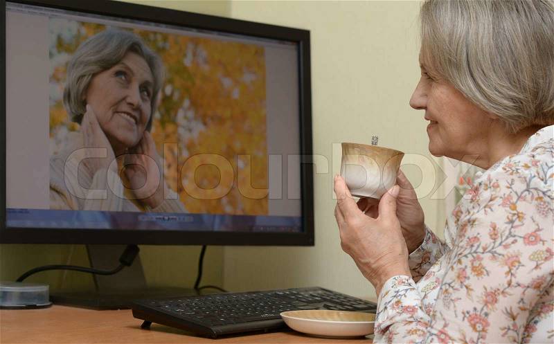 Mature woman relaxing at home watching pictures on computer, stock photo