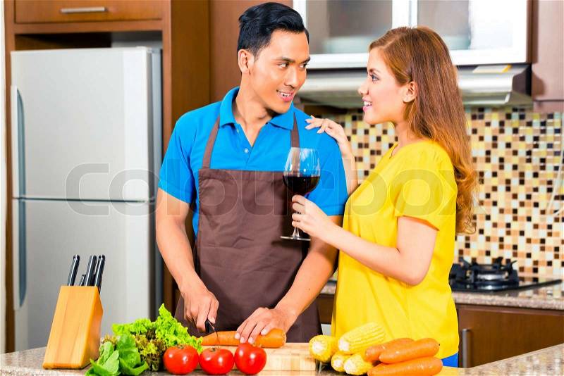 Asian couple cooking and cutting vegetables in domestic kitchen, drinking red wine, stock photo