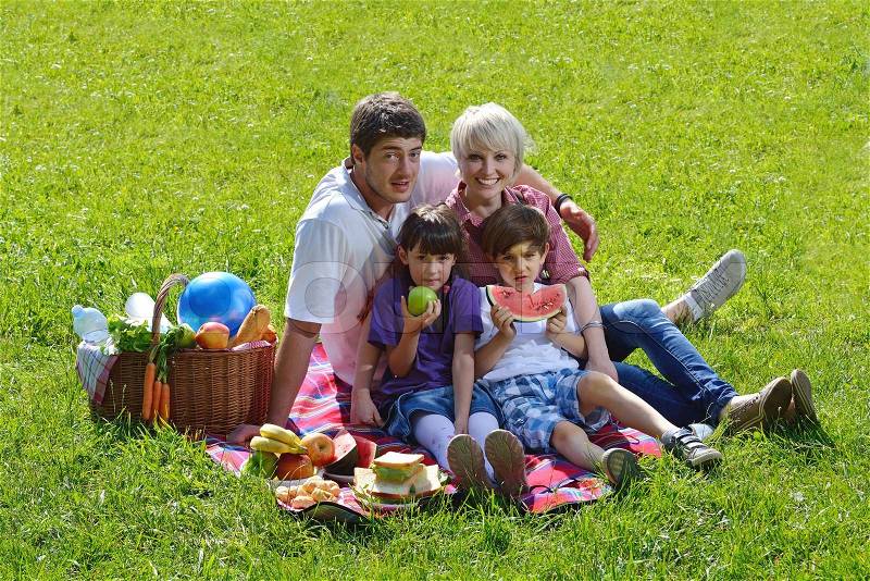 Happy young family playing together with kids and eat healthy food in a picnic outdoors, stock photo