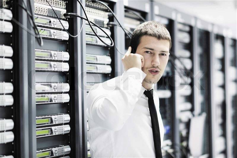 Young business man computer science engeneer talking by cellphone at network datacenter server room asking for help and fast solutions and services, stock photo