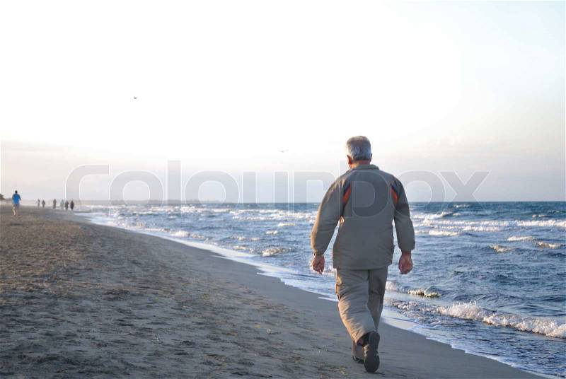 Lonely older man walking on beach, stock photo