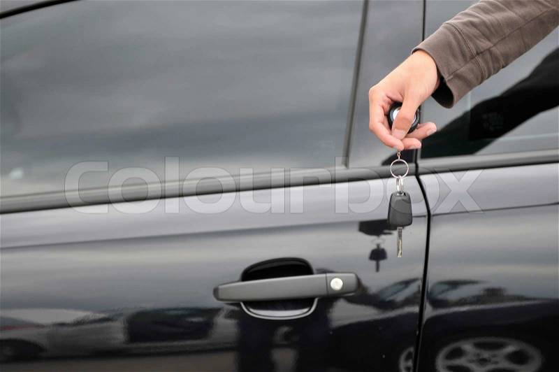 Male hand holding car key with new black car in background, stock photo