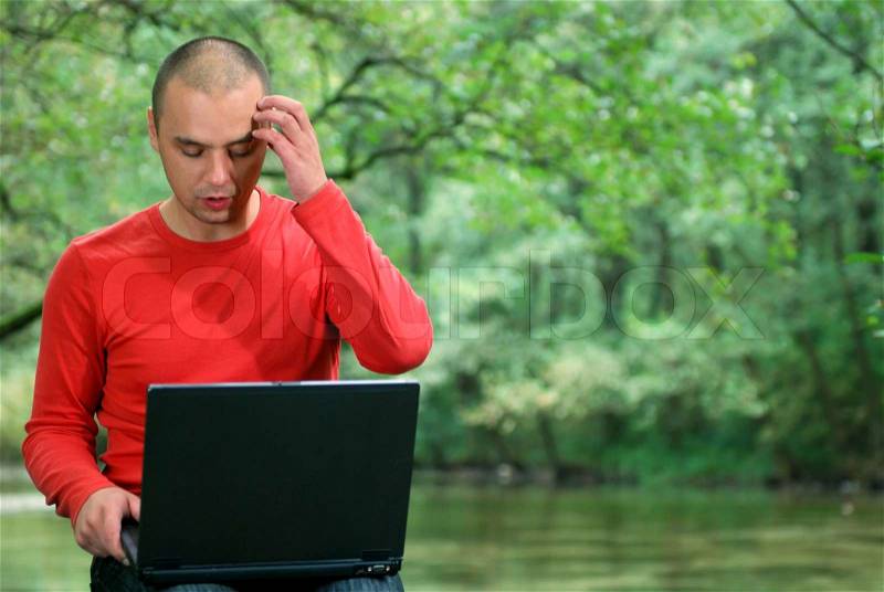 One young businessman working on laptop outdoor with green nature in background, stock photo