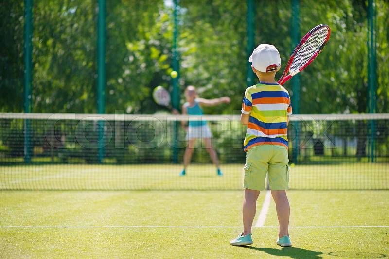 Little cute boy playing tennis on green court, stock photo