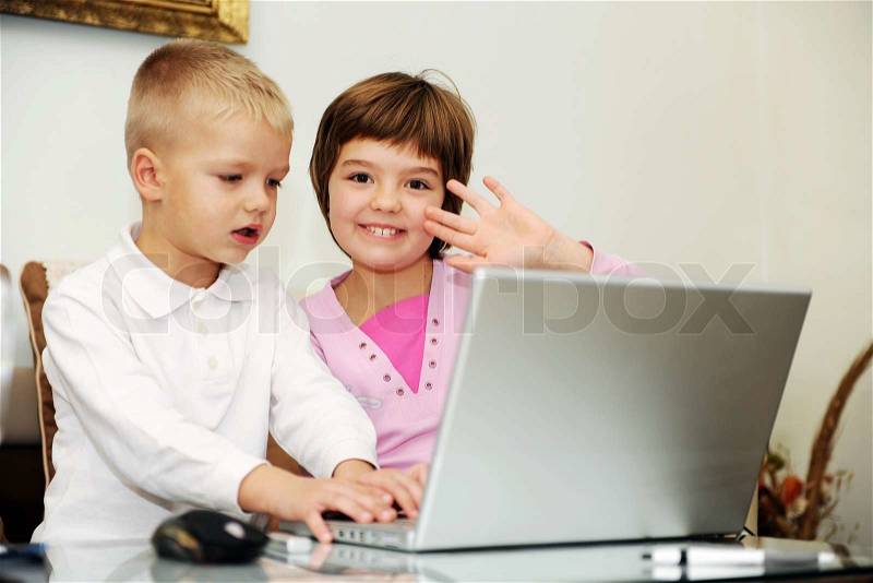 Two happy children playing games and learnig education lessons on laptop computer at home, stock photo