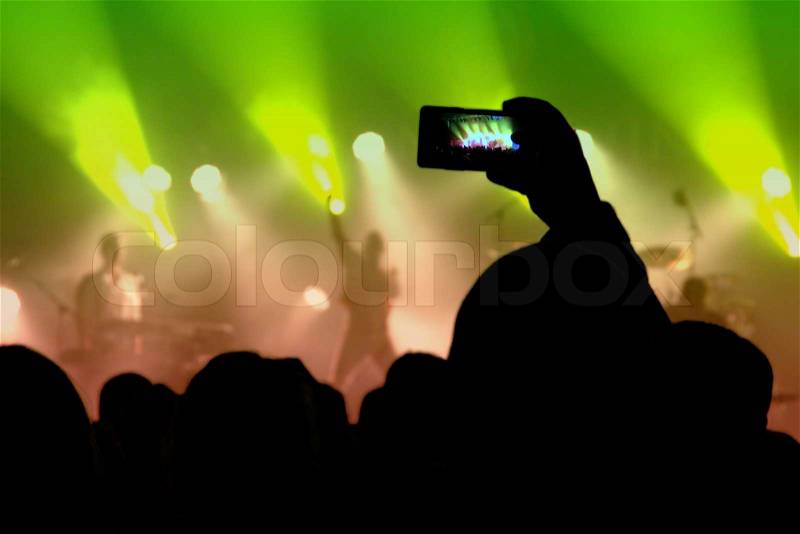 Crowd at concert with one person using smartphone, stock photo