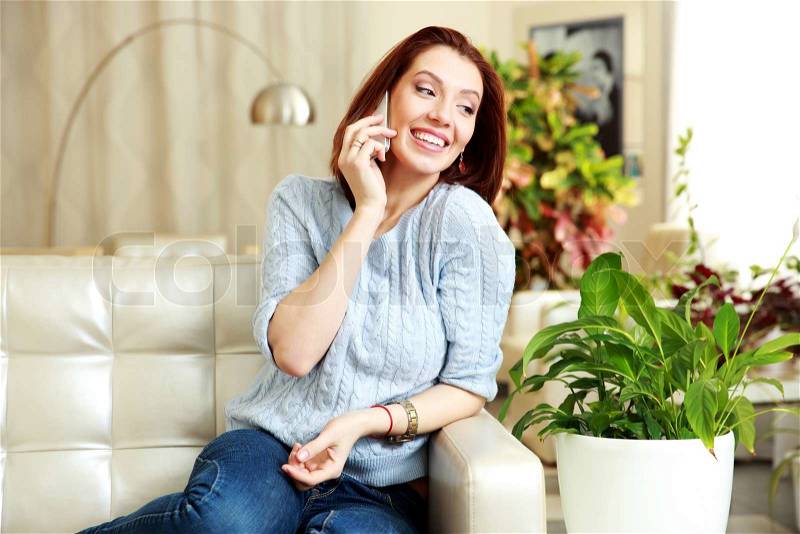 Happy woman talking on the phone and looking away at home, stock photo