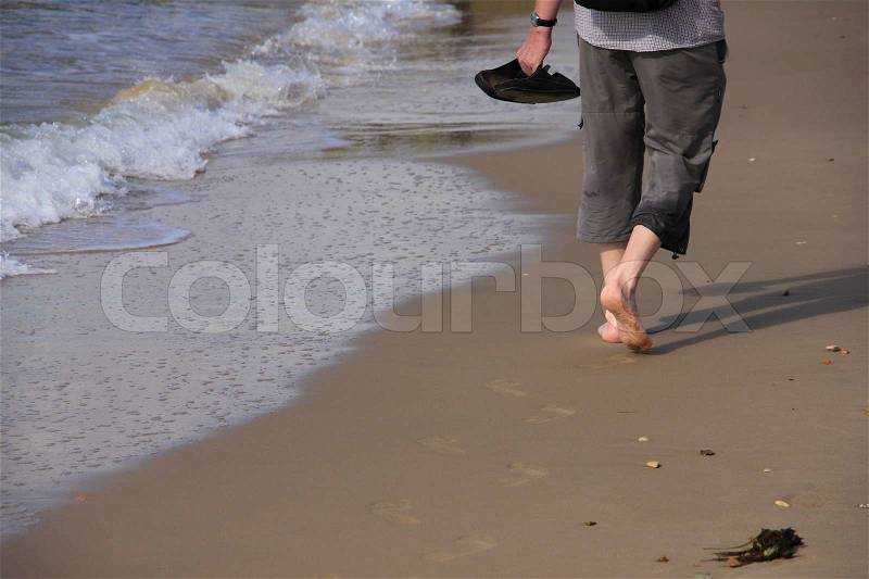 Man with bare feet and slippers in the hand is walking on the coastline near the sea, enjoy the summer, stock photo