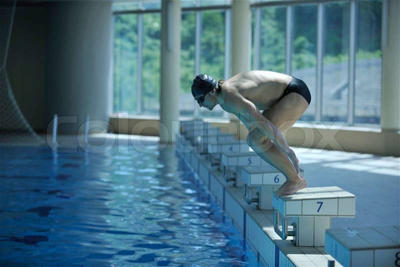 Young swimmer on swim start at swimming pool ready for jump race and win, stock photo