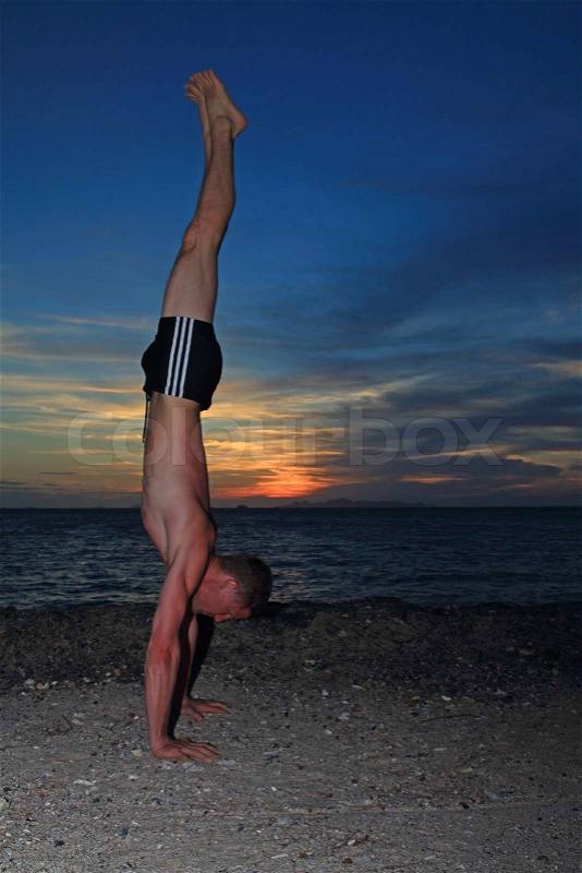 Man doing yoga Handstand pose by the beach at dusk, stock photo